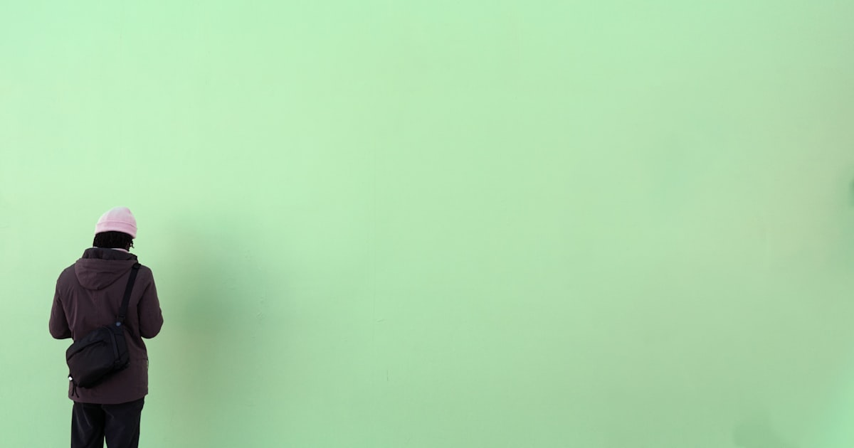 Person in pink hat stands against green wall