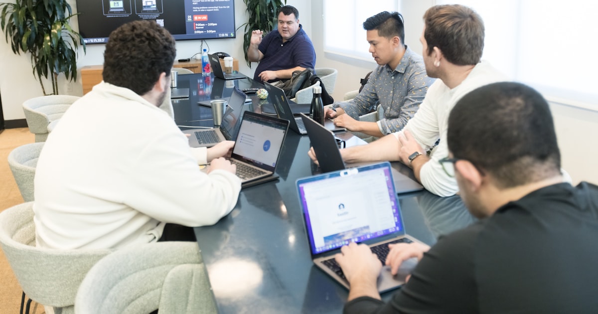 a group of men sitting around a table with laptops
