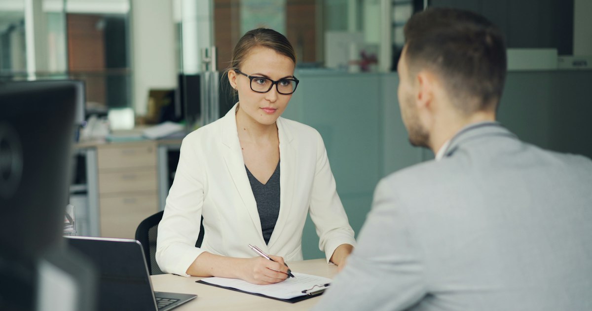 Woman in glasses interviews man at office desk