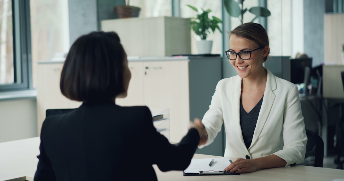 Two women shaking hands across a desk