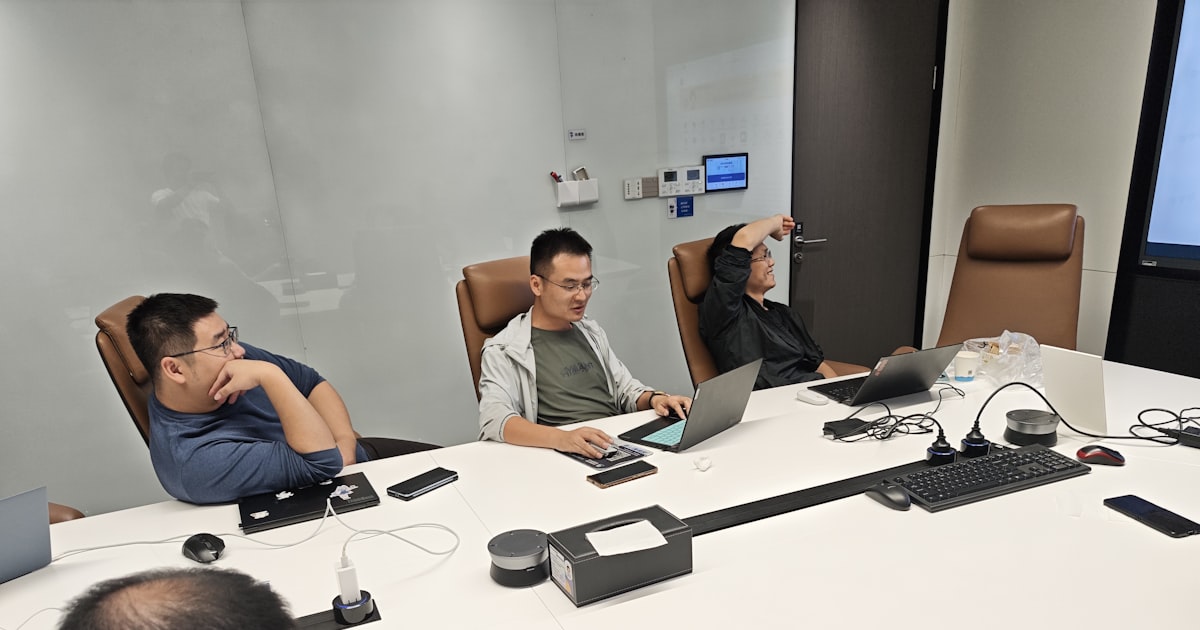Four men in a meeting room with laptops.