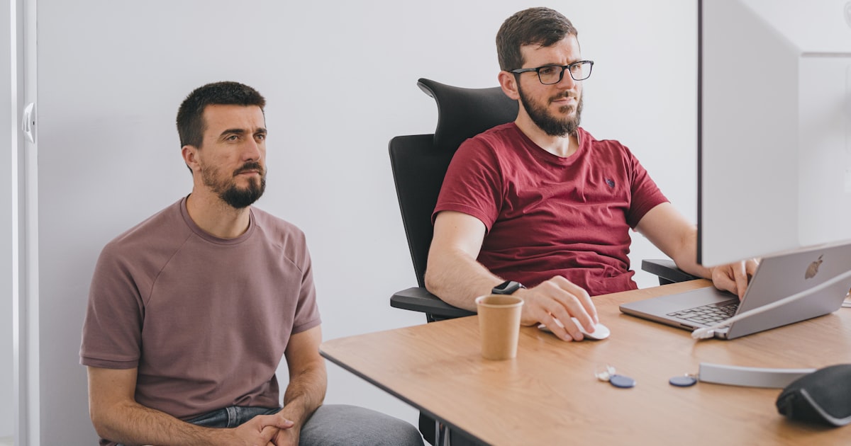 two men sitting at a table with a laptop