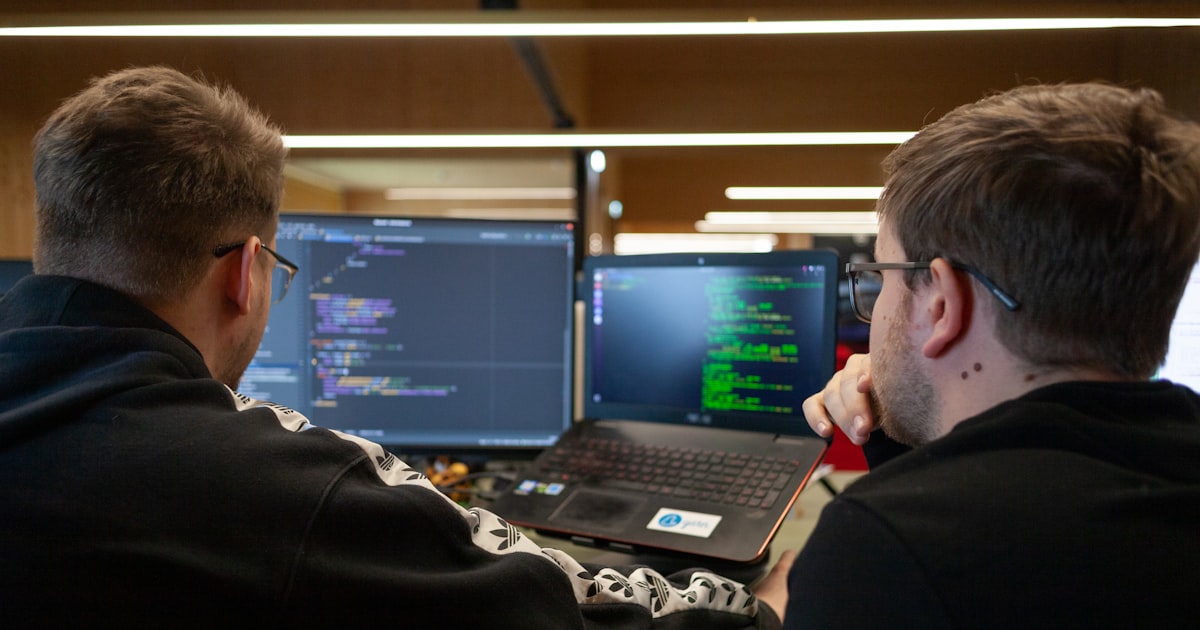two men sitting in front of a laptop computer